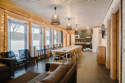 Aulangon Rantahuvilan pääsali. Etualalla sohvanurkkaus, keskellä maisemabaaritiski ja ruokailutila ja takana keittiönurkkaus ja käynti sähkösaunaosastoon.