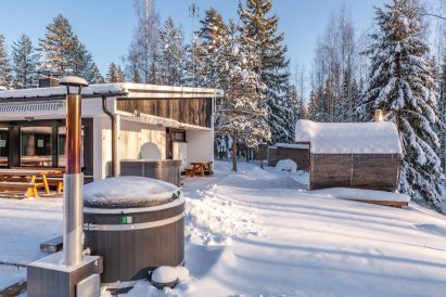 Lähdekallion Huvilan piha-alueen reunalla sijaitsevat puulämmitteinen kylpypalju ja erillinen puulämmitteinen tynnyrisauna. Terassilla näkyy ympärivuotinen sähköporeallas.