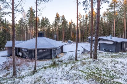 Talviaurinko laskee Lopen Erähuvilalla. Etualalla Kotahuvila, keskellä tulipaikka ja Minihuvila ja takana majoitusaitta ja kylpypaljut.